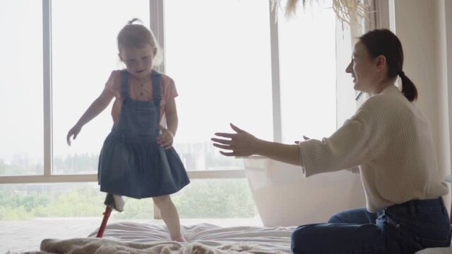kid with leg prosthesis having fun on bed with mother