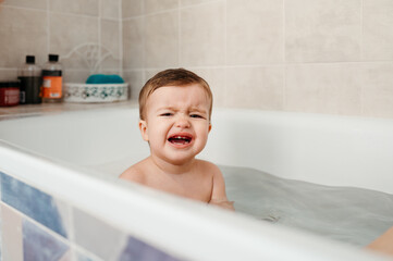 Capricious baby sitting in bathtub and crying