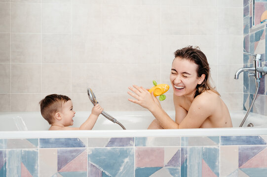 Happy baby pouring water on mother in bathtub