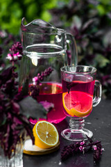 Tasty purple basil lemonade in glass with lemon and ice on a dark table in the summer garden. Picnic time with cold drink.