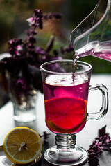 Tasty purple basil lemonade in glass with lemon and ice on a dark table in the summer garden. Picnic time with cold drink.
