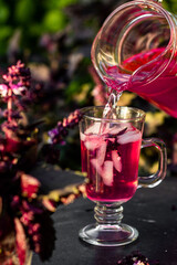 Tasty purple basil lemonade in glass with ice on a dark table in the summer garden. Picnic time with cold drink.