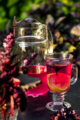 Tasty purple basil lemonade in glass with lemon and ice on a dark table in the summer garden. Picnic time with cold drink.