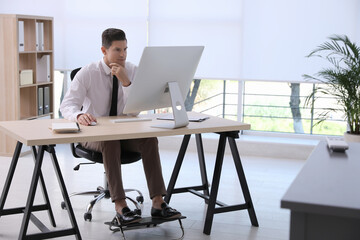 Man using footrest while working on computer in office - obrazy, fototapety, plakaty