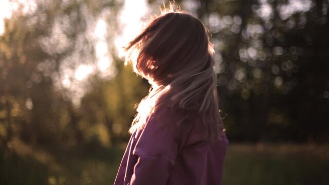 Attractive fashion model with flying hair in the garden in the summer time. Young beautiful blonde woman shakes hair. Blossoms fall from trees. Slow motion