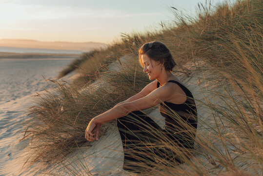 Woman sitting in the sand dunes at the beach during sunset