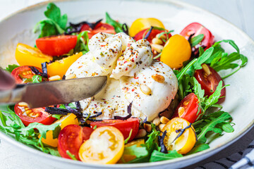 Close-up of burrata cheese salad with arugula, nuts and tomatoes.
