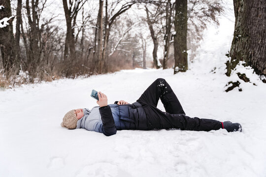 Boy lying in the snow looking at his mobile phone