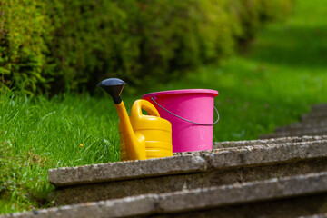 Plastic garden pink watering can stands on freshly plowed ground
