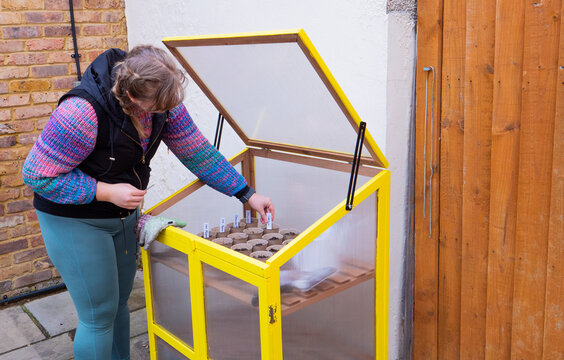 Girl placing name tag into pots freshly seeded inside a yellow greenhouse