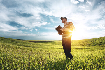 A young agronomist holds a folder in his hands on a green wheat field. A farmer makes notes on the...