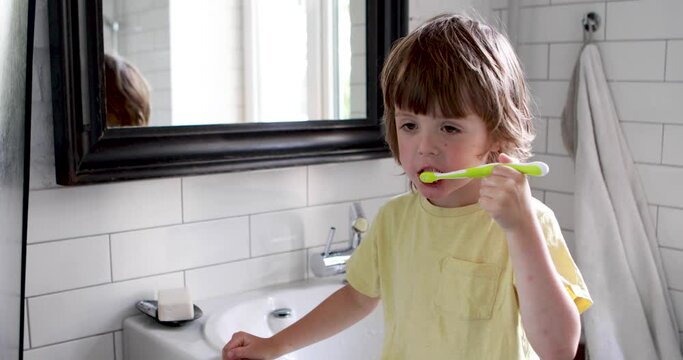 Cute boy with brushing his teeth with a toothbrush and looking at camera in bathroom. Dental health care