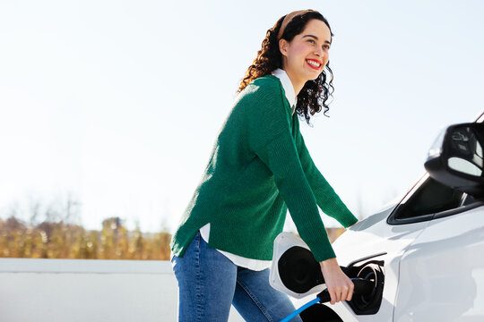Cheerful female driver recharging electric car