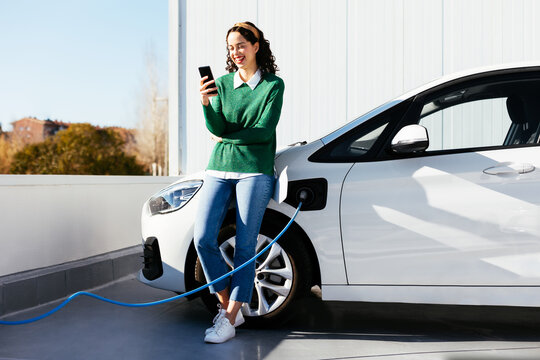 Woman using smartphone near electric car on charging station
