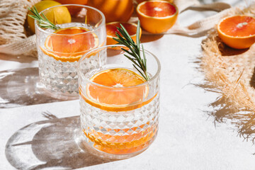Summer orange cocktails with fresh citrus fruits on white background. Hard seltzer, lemonade, refreshing drinks, low alcohol mocktails, summer party concept. Palm shadow and sunlight. Copy space.