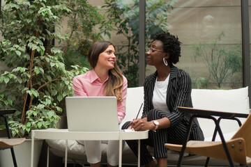 Two female colleagues are discussing some new business plans while sitting in the foyer of the company's building.