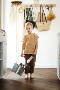 Toddler boy walking in the kitchen with tin bucket full of cleaning products