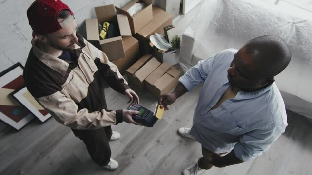 High angle shot of male African-American homeowner using debit card to pay for services of moving company