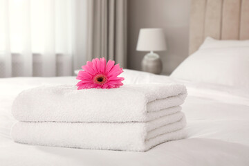 Fototapeta na wymiar Stack of fresh towels with flower on bed indoors