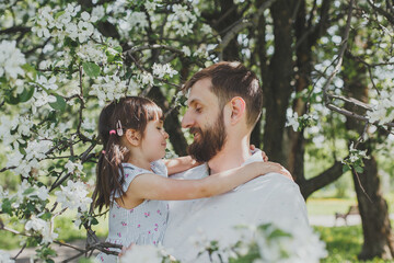 cute portrait of dad and little daughter in a blooming garden, father's day holiday concept 