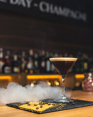 beautiful glass with cocktail decorated with blooming twig and mixing stands on the bar. Blurred background