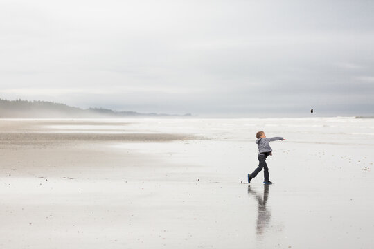 Boy throws rock on cloudy beach