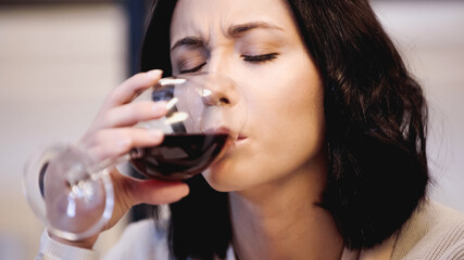 close up view of upset woman drinking red wine from glass with closed eyes at home