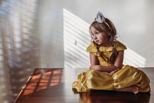 Young girl in costume dress sitting in window light at home