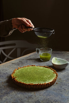 woman sprinkles matcha tea onto green cheesecake