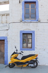 Fototapeta na wymiar Yellow motorcycle near white building with blue window frames in the Greek style. Travel and architecture concept. Bodrum, Turkey