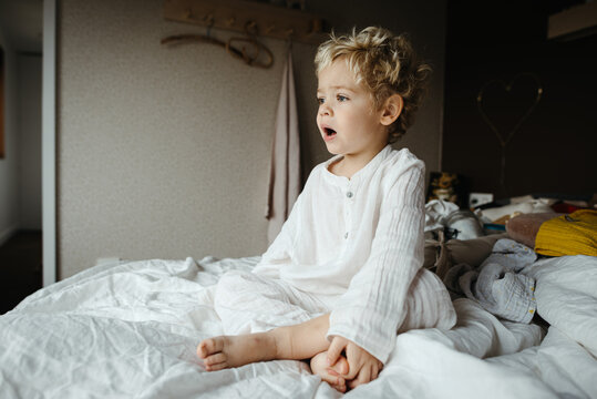 Toddler boy sitting on a messy double bed
