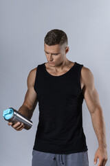 Man wearing blank black tank top is drinking protein or other supplement from a metal shaker