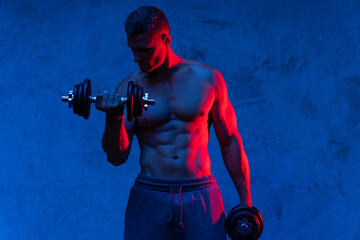 Muscular bodybuilder man exercising with dumbbells in colorful neon light