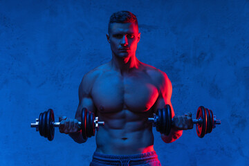 Muscular bodybuilder man exercising with dumbbells in colorful neon light