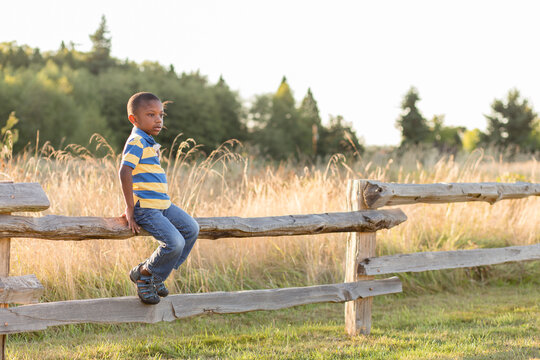 Black boy perches on split rail fence
