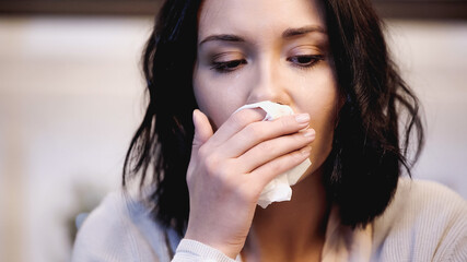 close up view of upset woman wiping nose with paper napkin at home
