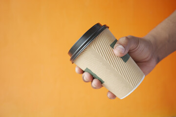 hand holding take away paper cup against orange background.