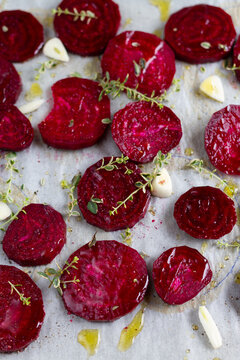 Slices of raw beet on baking tray sprinkled with thyme, garlic and olive oil