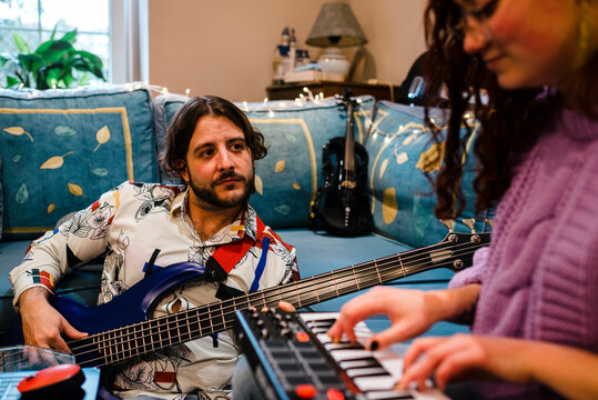 Musician playing bass guitar close to his partner at home studio