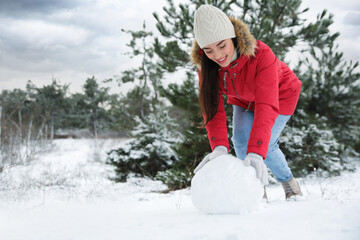 Young woman rolling snowball outdoors on winter day. Space for text