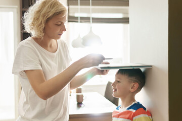 Mother playfully measuring the height of her son at home