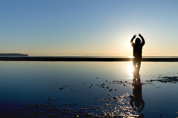 Boy jumps with hands in air at sunset beach