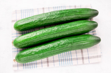 three cucumbers on a kitchen towel against a white background