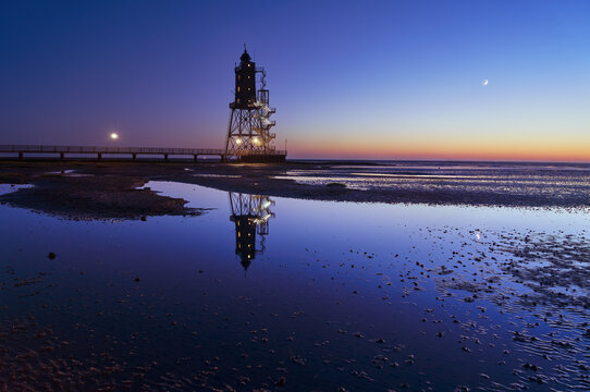 scenic night view of the historic lighthouse "Obereversand" in Dorum-Neufeld (Germany) during the blue hour at low tide while it is reflected in the remainig water of the North Sea