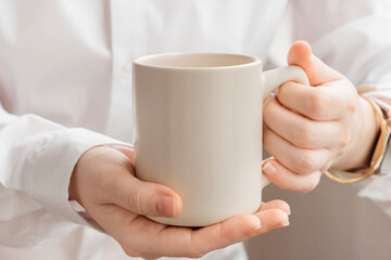 Big white mug for hot tea in human hands above white background. Holding hands with cup mock up with empty space for your design.