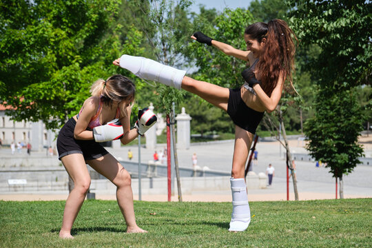 Two women practicing muay thai, boxing, kickboxing, in a park. Sport outdoors.