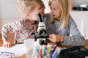 young girl and little sister looking through microscope 