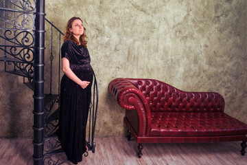 Leather sofa with a black spiral staircase and a pregnant woman stands in a long evening dress