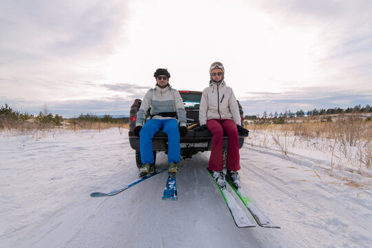 Winter fun: couple sitting in the trunk of a car wearing skis 