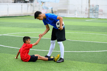 Asian teenager Football Players pulls the hand of a fallen player. - obrazy, fototapety, plakaty